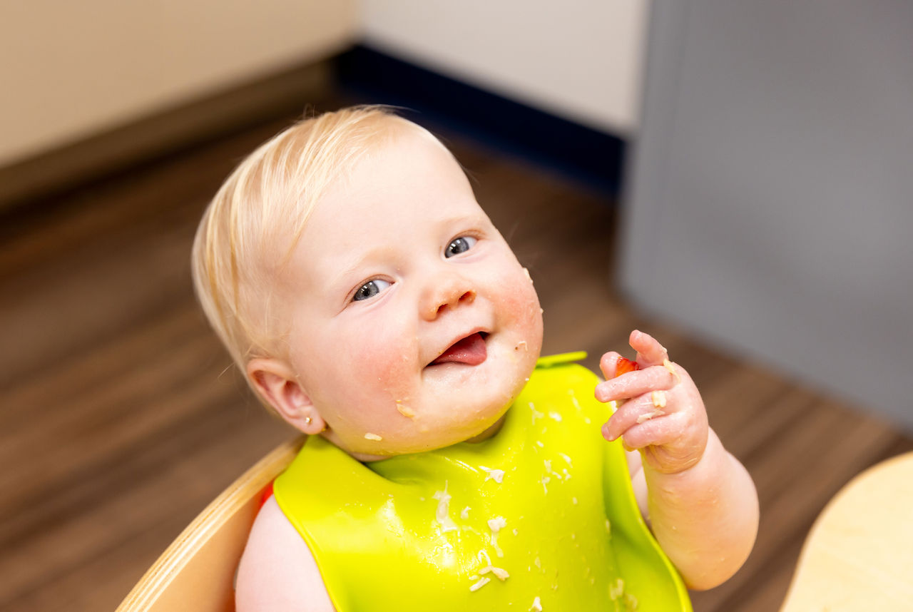 Your Comprehensive Guide to Picky Eating A cute smiling baby wearing a bright green bib with food on his hand, face and bib