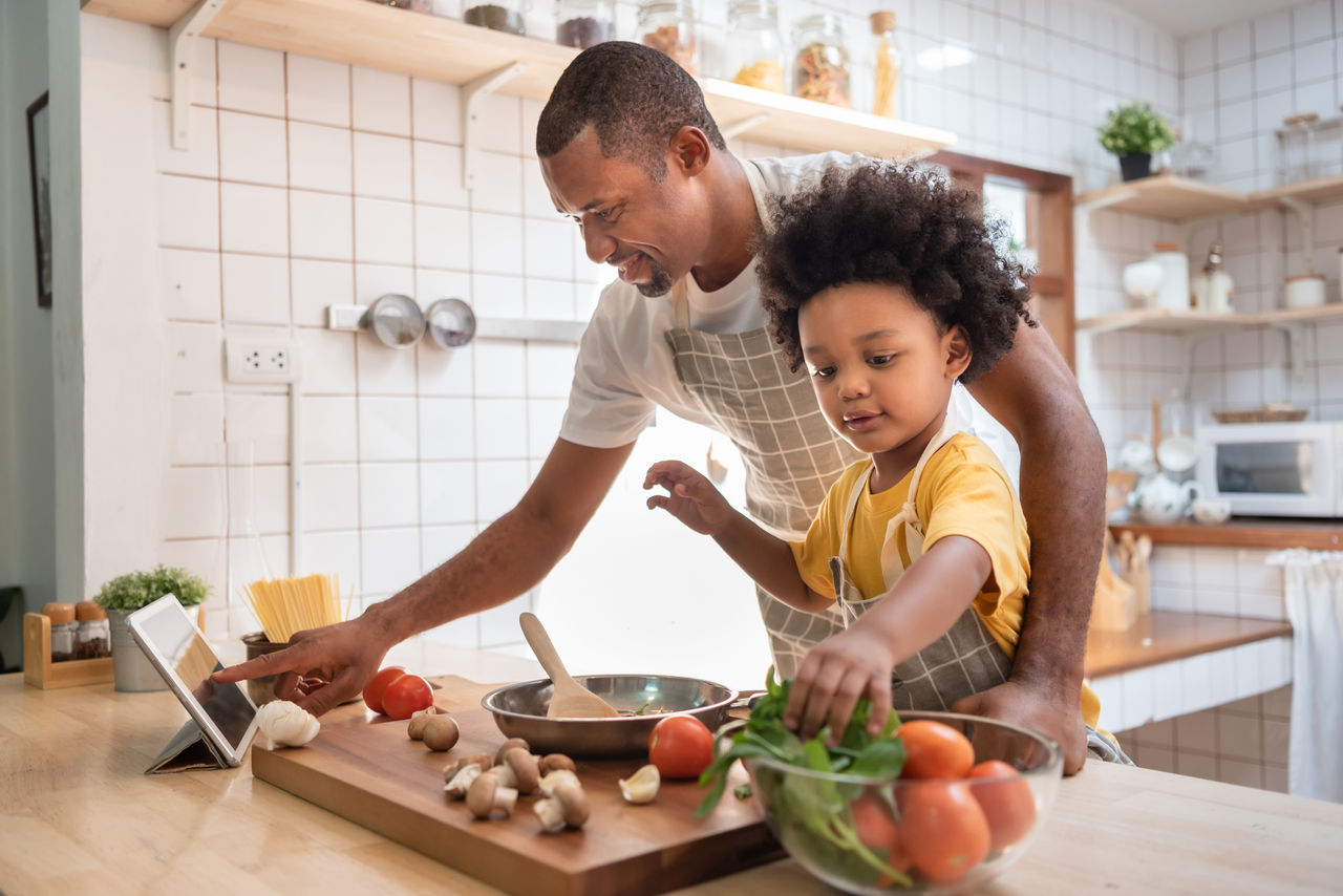 Cooking with Kids: Fun, Age-Appropriate Tips to Build Skills A father and daughter cooking together at an island in the kitchen with vegetables and pasta