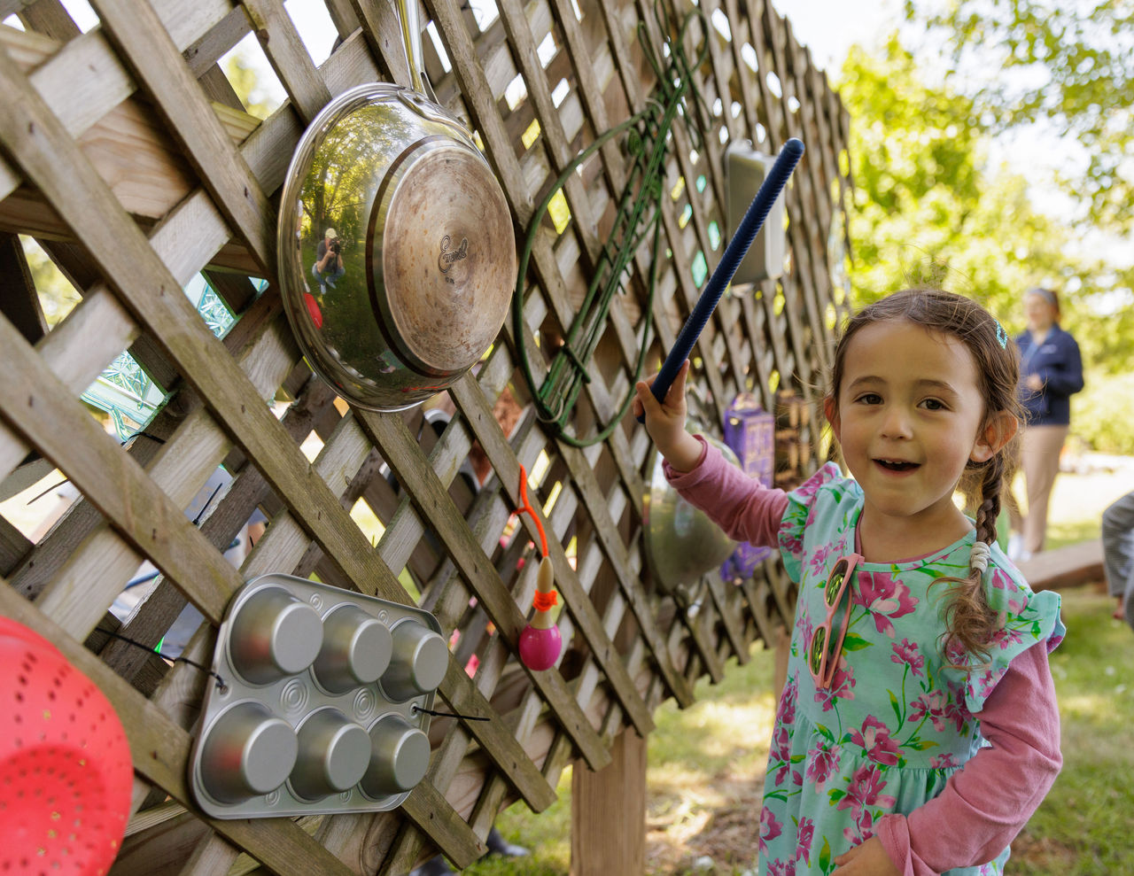 5 Tips To Encourage Play Without Screen Time A child playing outdoors on a music wall created out of found objects like a muffin tin, colander and metal pot