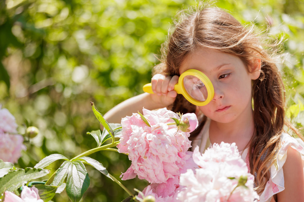 Learning More About Your Child Through Observation A young girl outdoors looking at a pink flower through a yellow magnifying glass