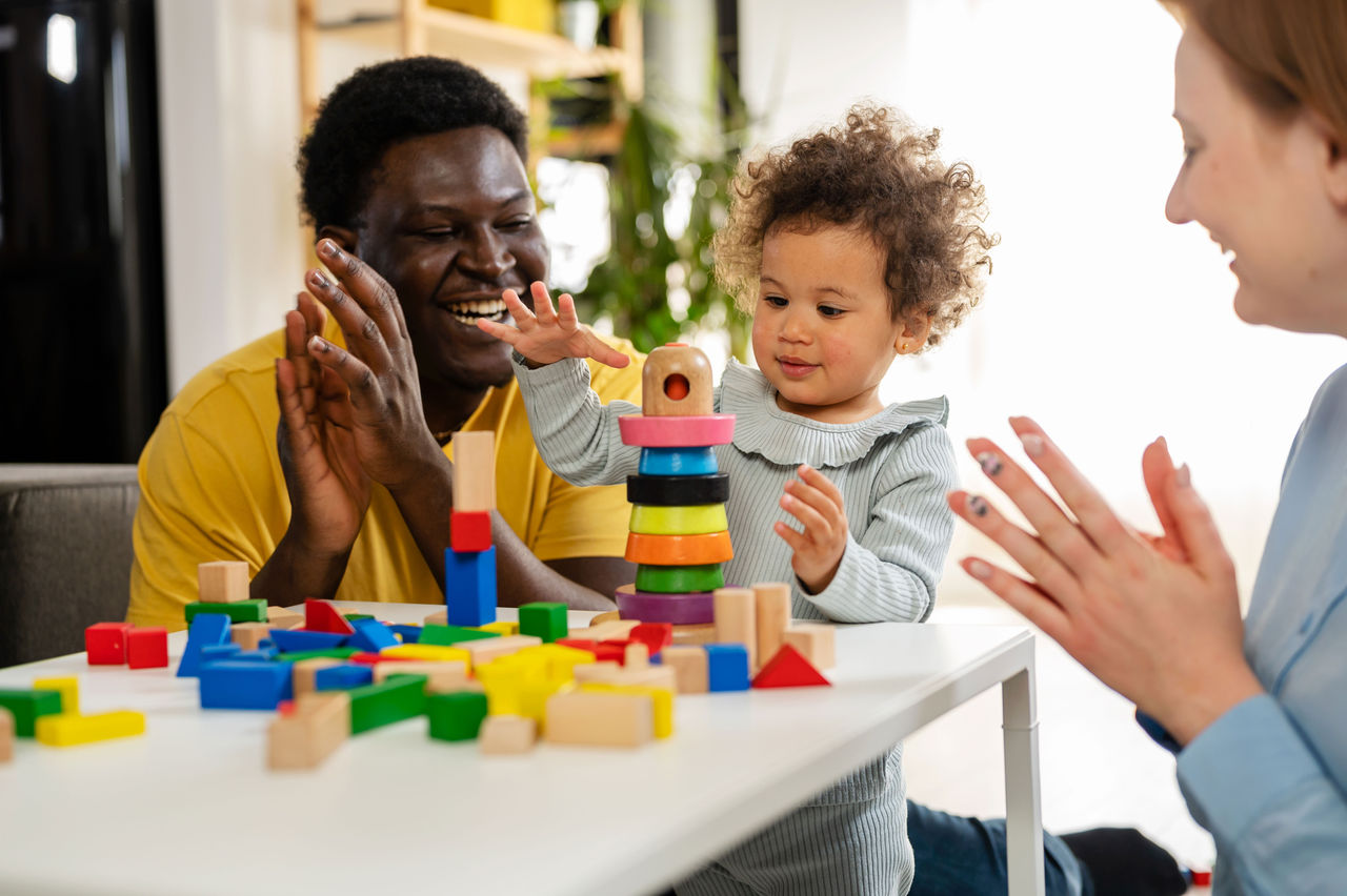 The Home-School Connection: Learning at Home Parents cheering on their baby who is stacking blocks at a table in their home